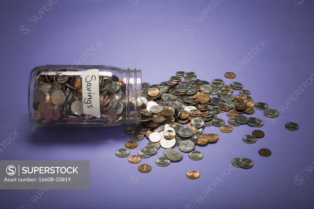 Glass jar with coins and Savings label and scattered coins
