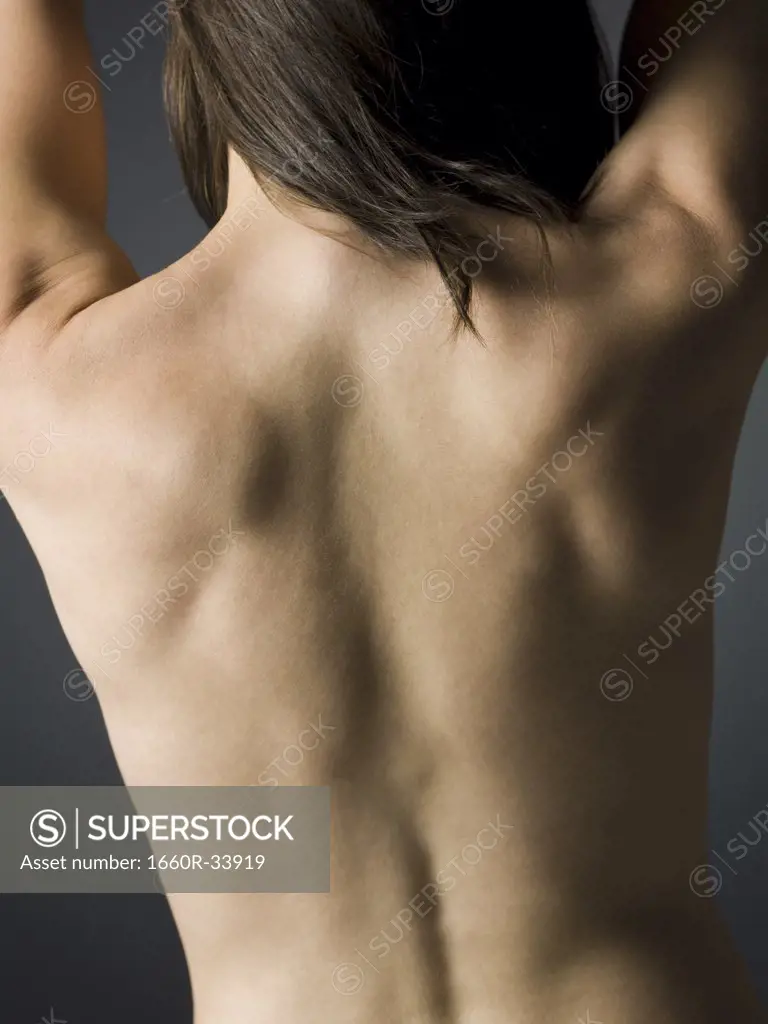 Rear view of topless woman with hands on lower back waist up
