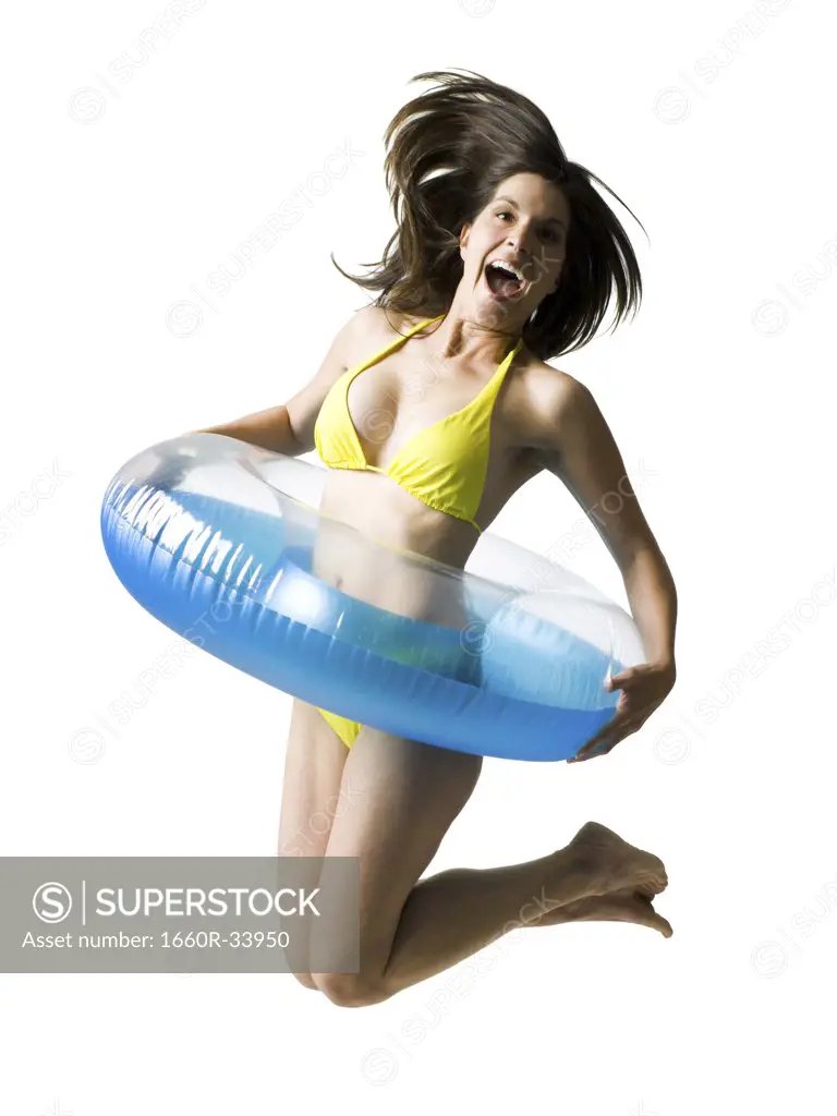 Woman in bikini with swimming ring around waist jumping and smiling
