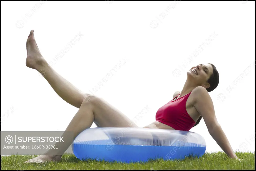 Woman sitting in swimming ring on grass with leg up smiling