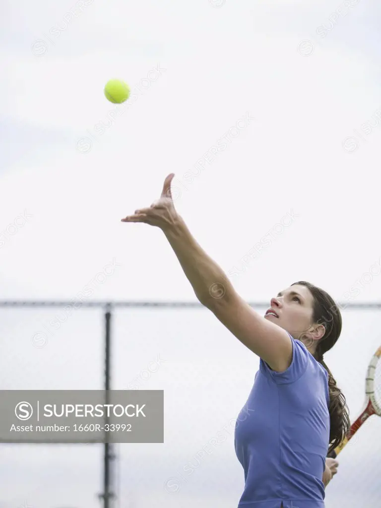 Woman tossing tennis ball in air to serve