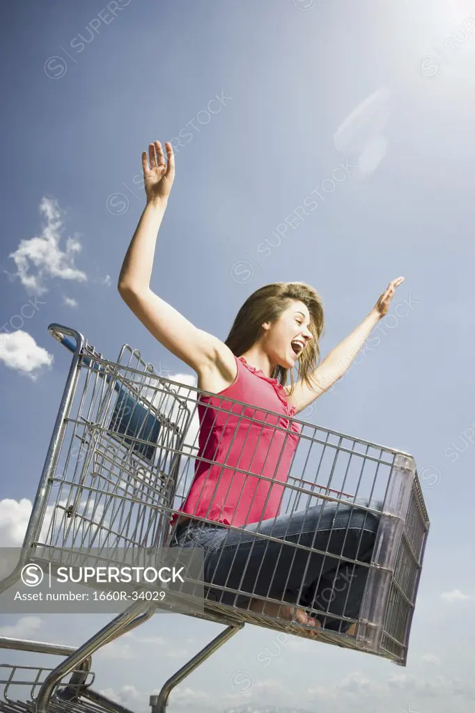 Woman in shopping cart outdoors with arms up smiling