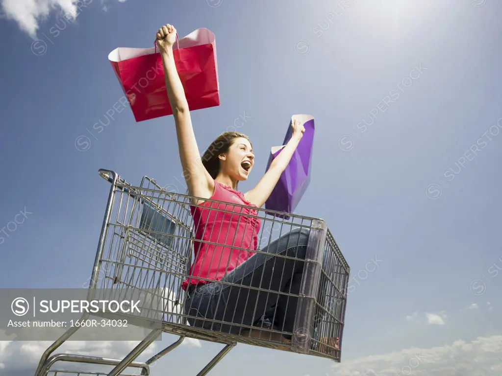 Woman in shopping cart outdoors with shopping bags smiling