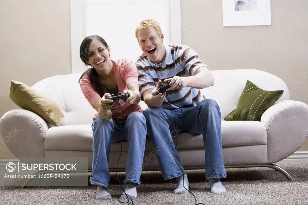 Man and woman sitting on sofa playing video games laughing