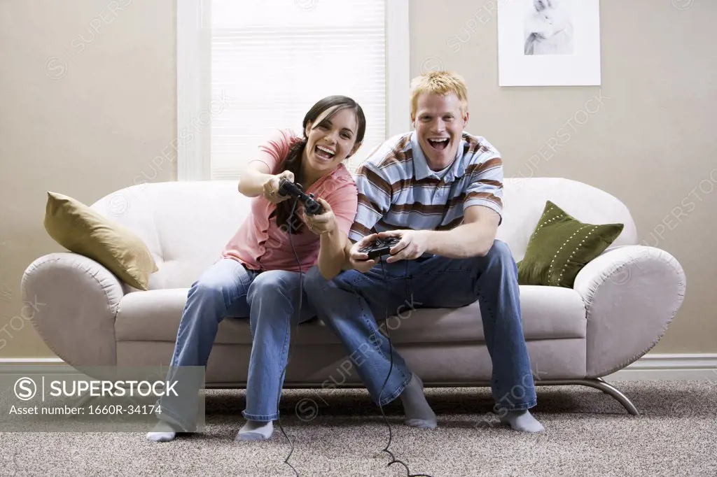 Man and woman sitting on sofa playing video games laughing