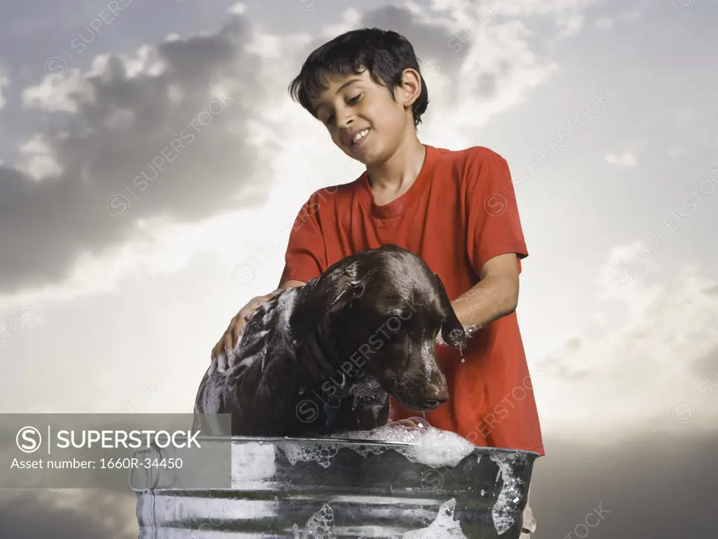 Boy bathing dog outdoors on cloudy day