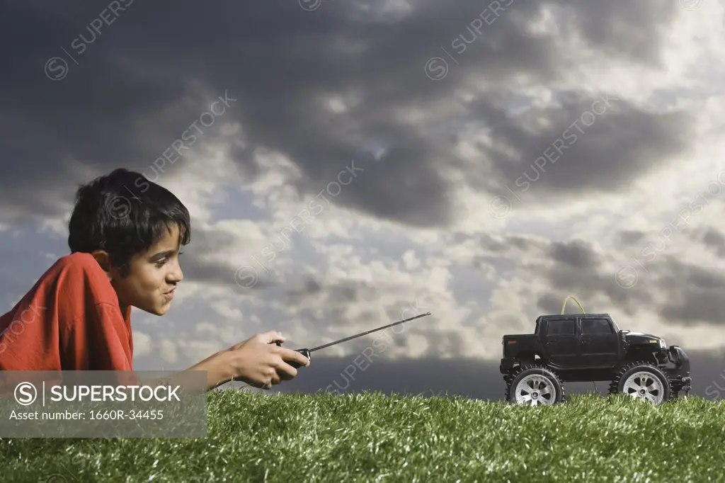 Boy playing with remote controlled truck outdoors on lawn on cloudy day
