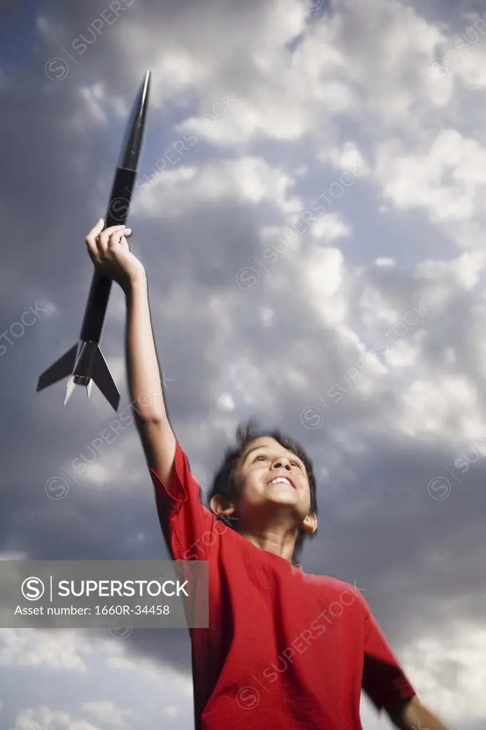 Boy playing with toy rocket outdoors on cloudy day low angle view