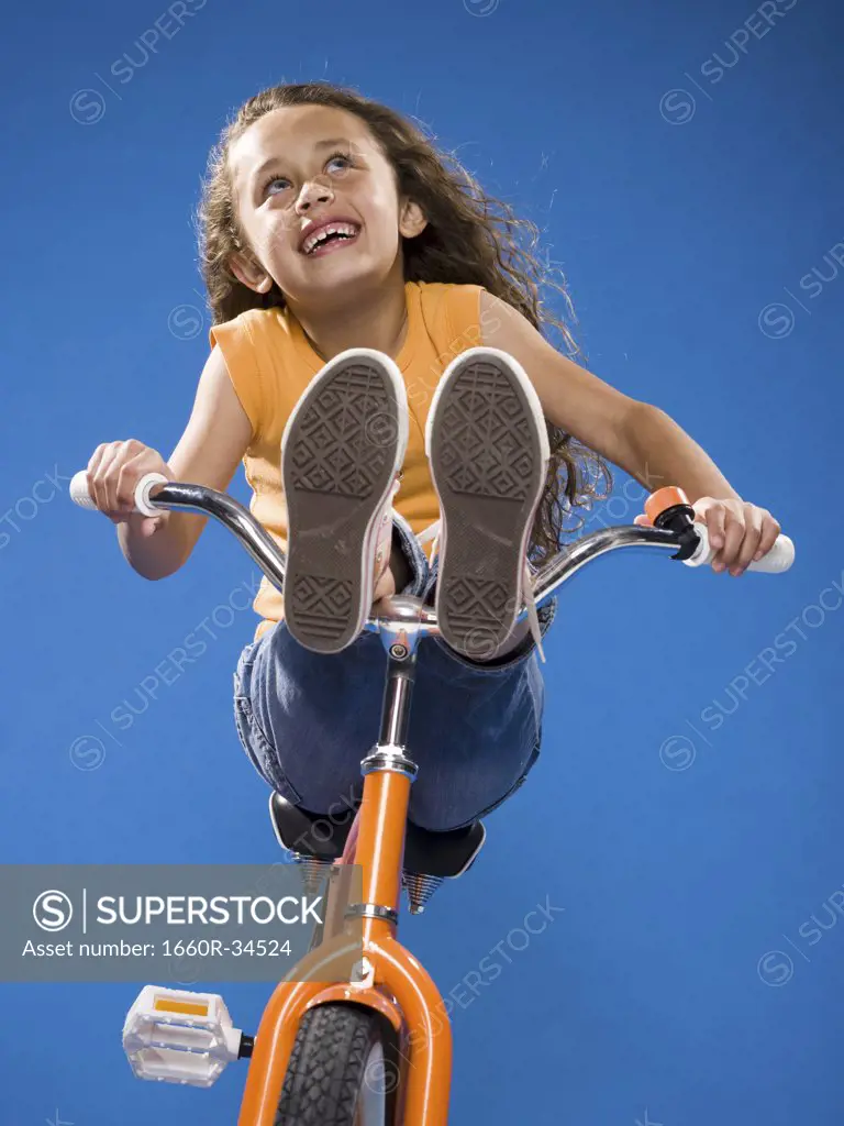 Girl riding orange bicycle with feet on handlebars smiling