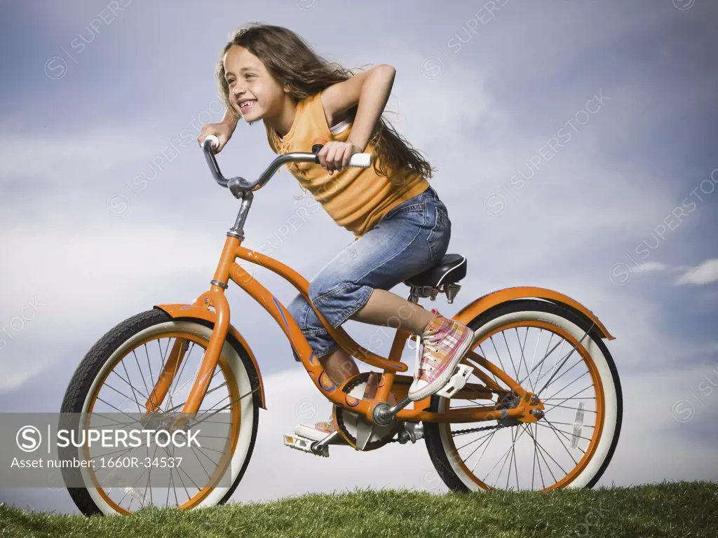 Girl sitting on orange bicycle outdoors smiling
