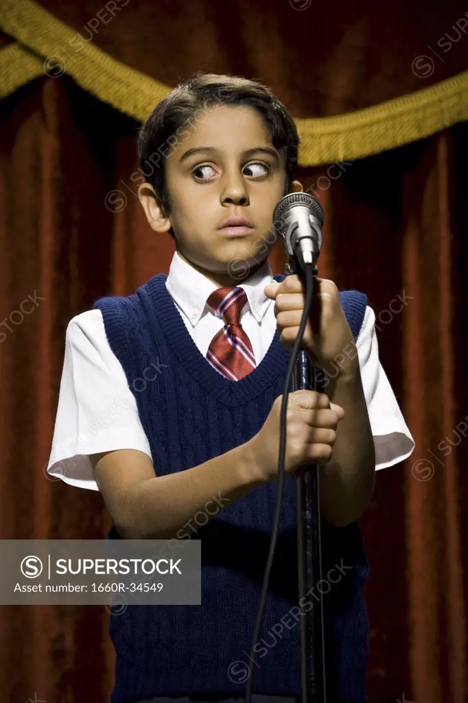 Boy standing on stage with microphone and big eyes