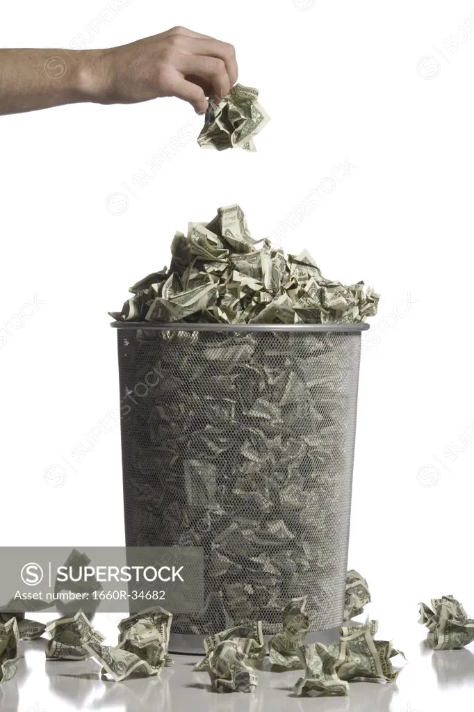 Person throwing crumpled money into waste paper basket