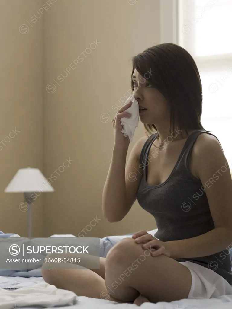 Woman sitting cross legged on bed blowing nose