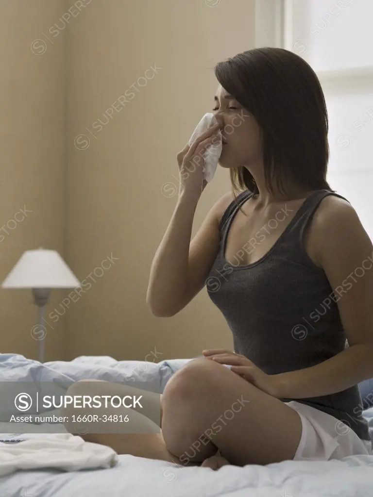 Woman sitting cross legged on bed blowing nose