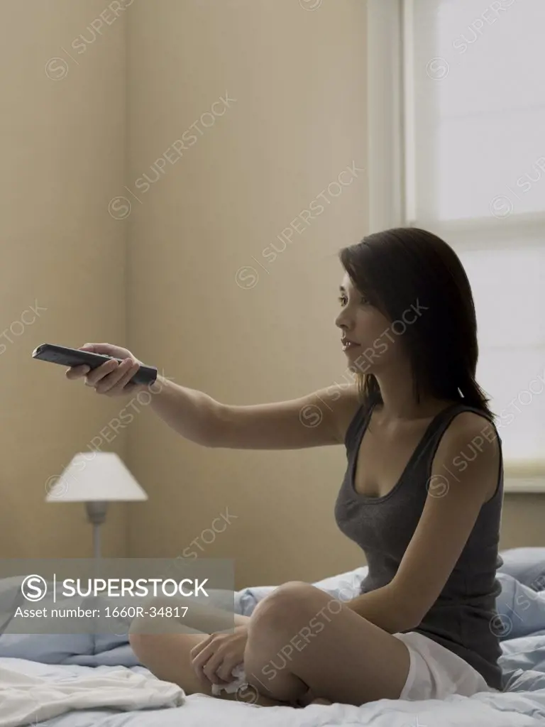 Woman sitting on bed with television remote and tissue