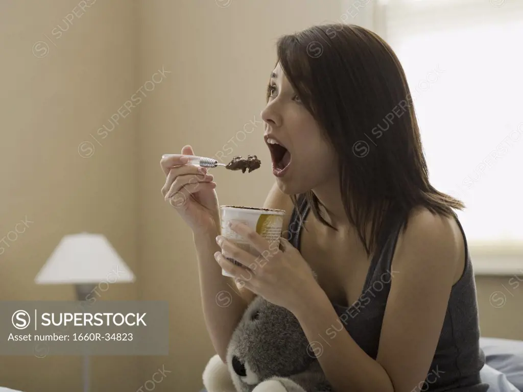 Woman eating chocolate ice cream in bed with stuffed animal