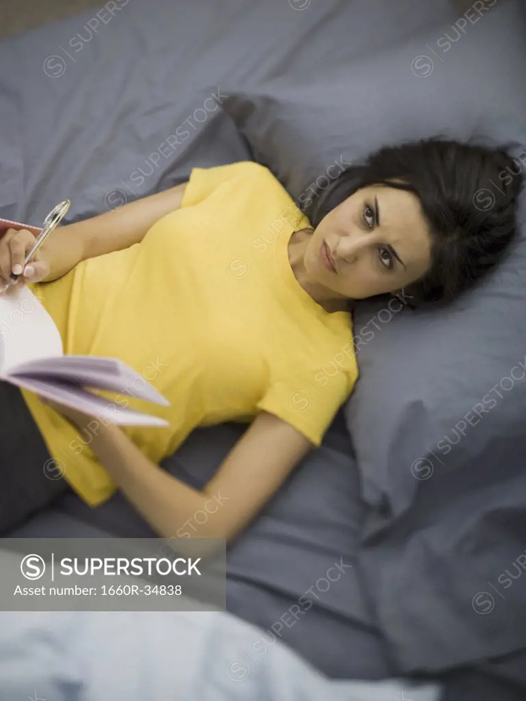 Woman in bed with notebook and pen smiling