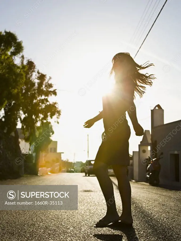 Woman standing on street in silhouette with arms up backlit