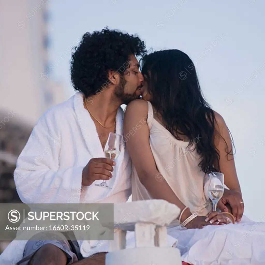 Couple sitting outdoors with champagne flutes and scenic background smiling and snuggling