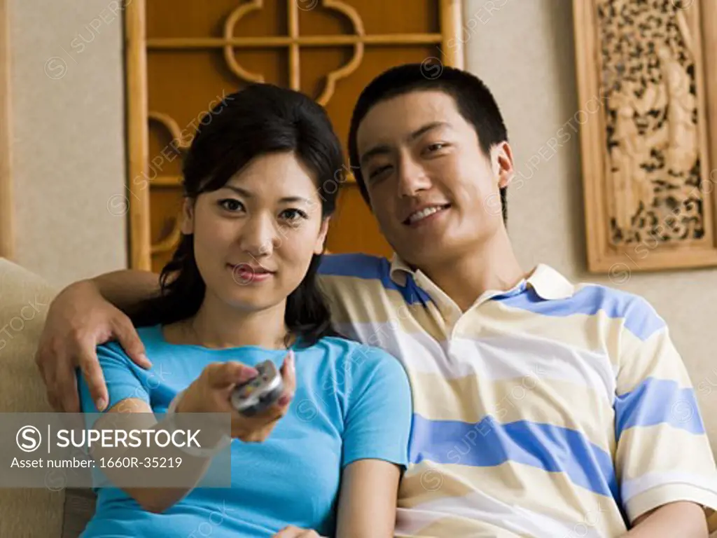 Couple embracing on sofa while woman changes channels with television remote
