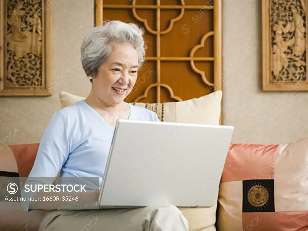 Woman sitting on sofa with laptop smiling