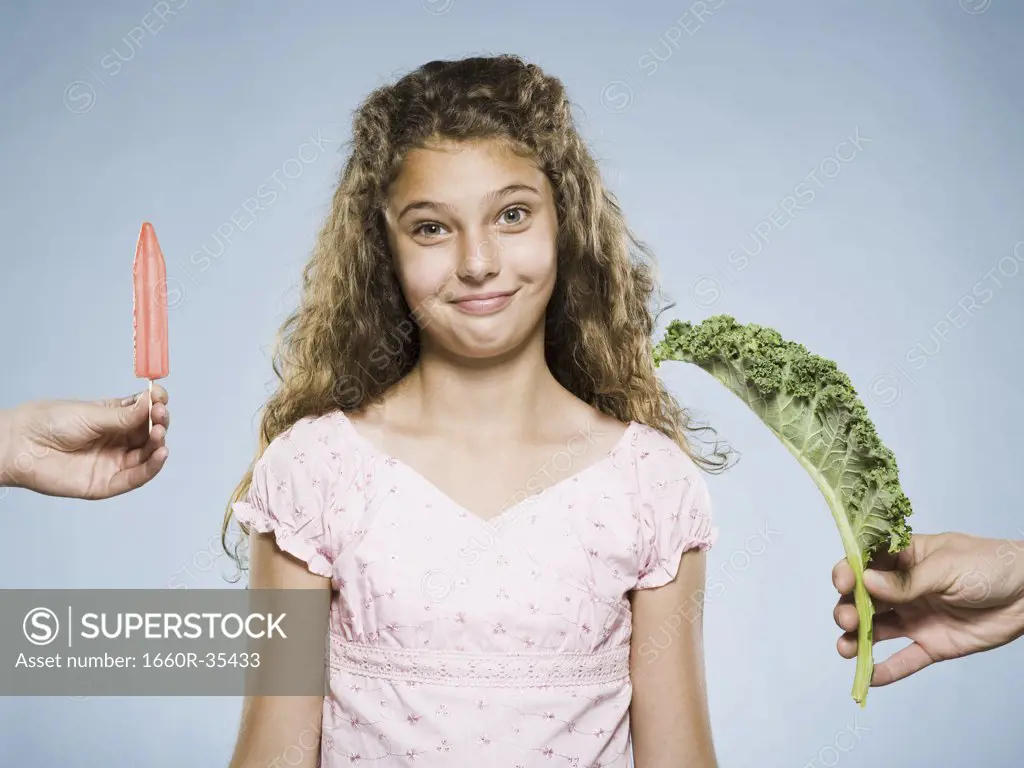Girl deciding between Popsicle and green leafy vegetable