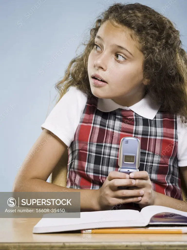 Girl sitting at desk with workbook hiding cell phone
