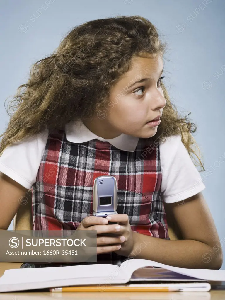 Girl sitting at desk with workbook hiding cell phone