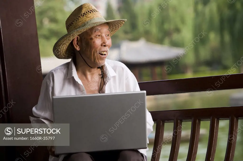 Mature man with straw hat and laptop outdoors