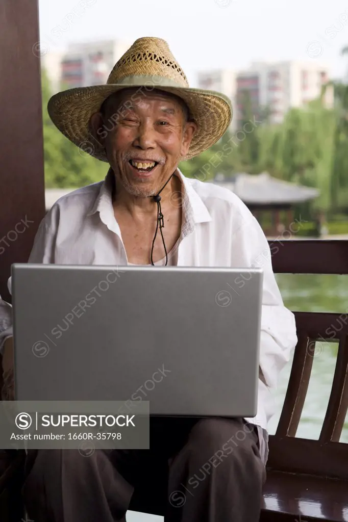 Mature man with straw hat and laptop outdoors