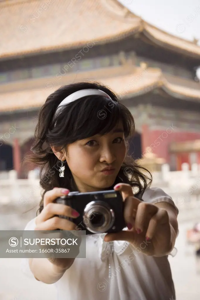Teenage girl taking photograph outdoors with pagoda in background