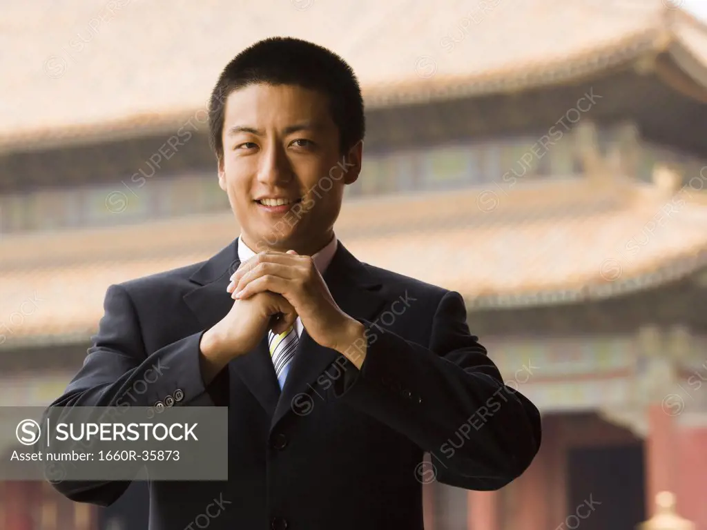 Businessman smiling with hands in greeting with pagoda in background
