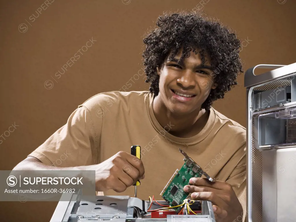 young man in a brown shirt fixing a computer.