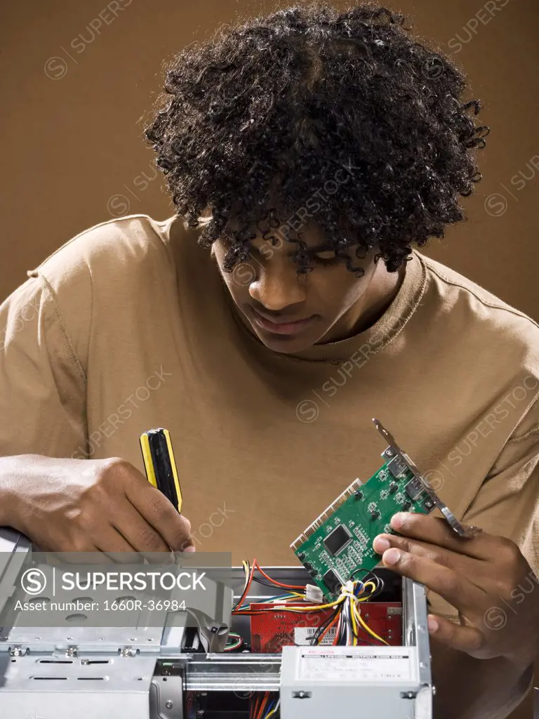 young man in a brown shirt fixing a computer.
