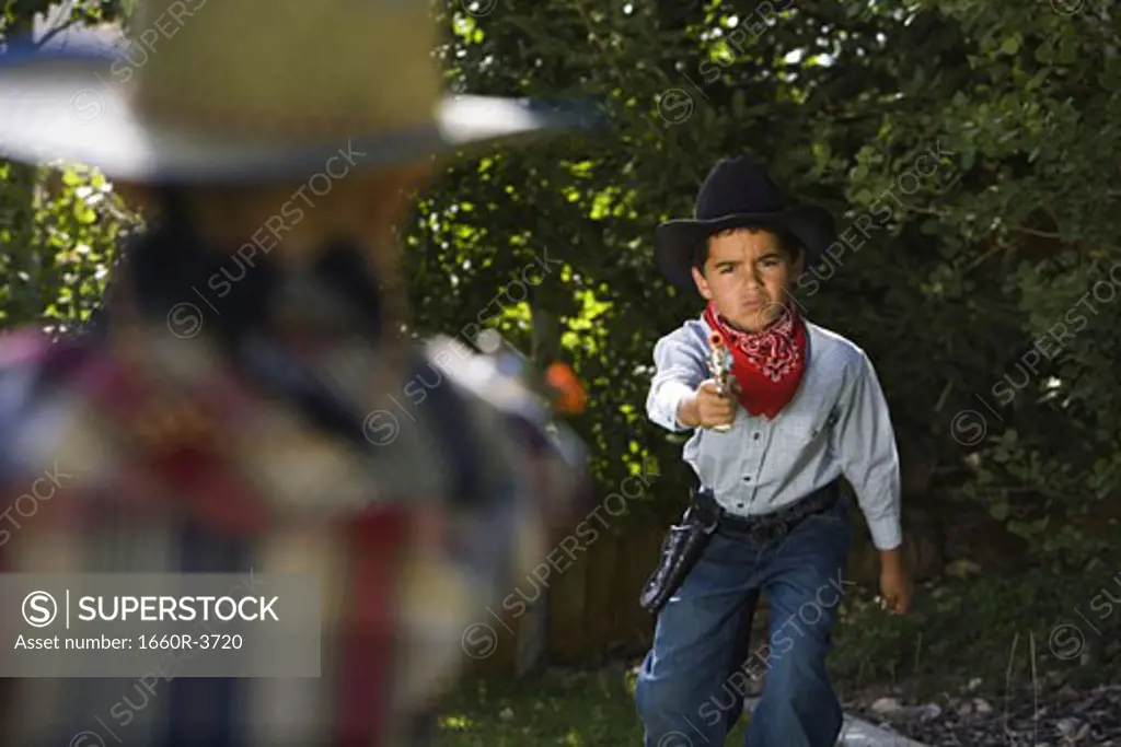 Two boys in cowboy costumes aiming each other with a toy gun