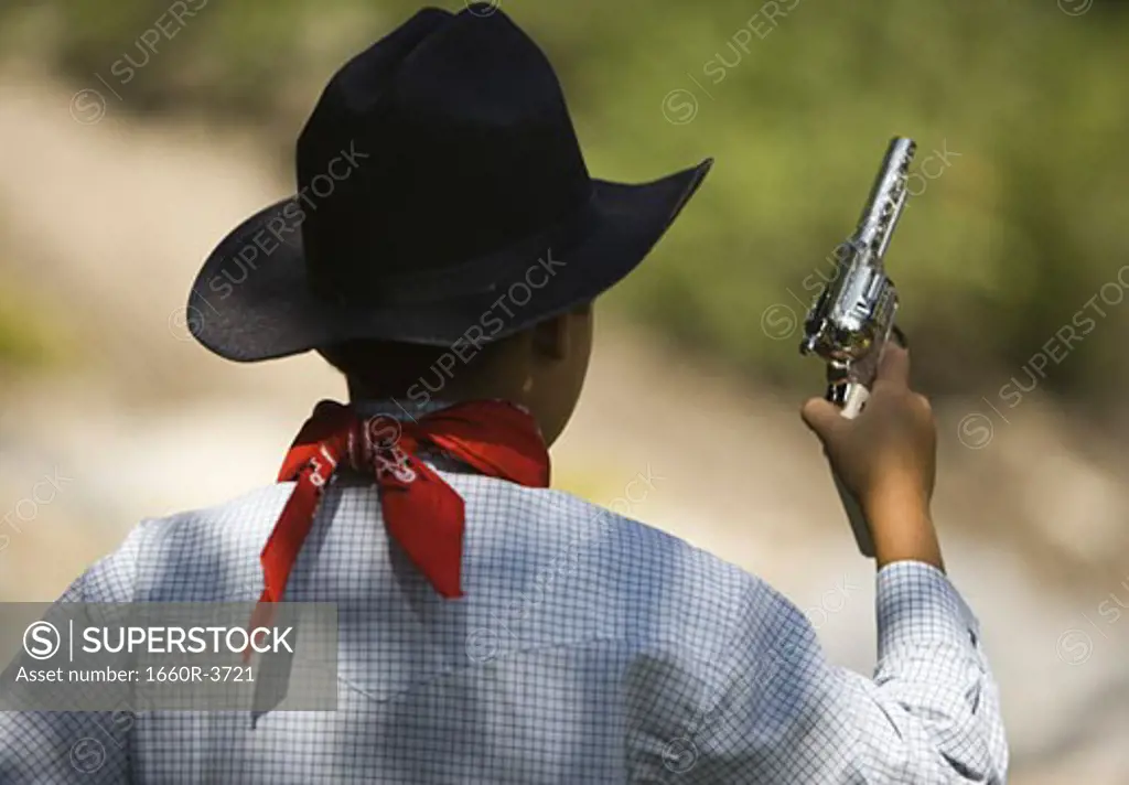 Rear view of a boy in a cowboy costume holding a toy gun