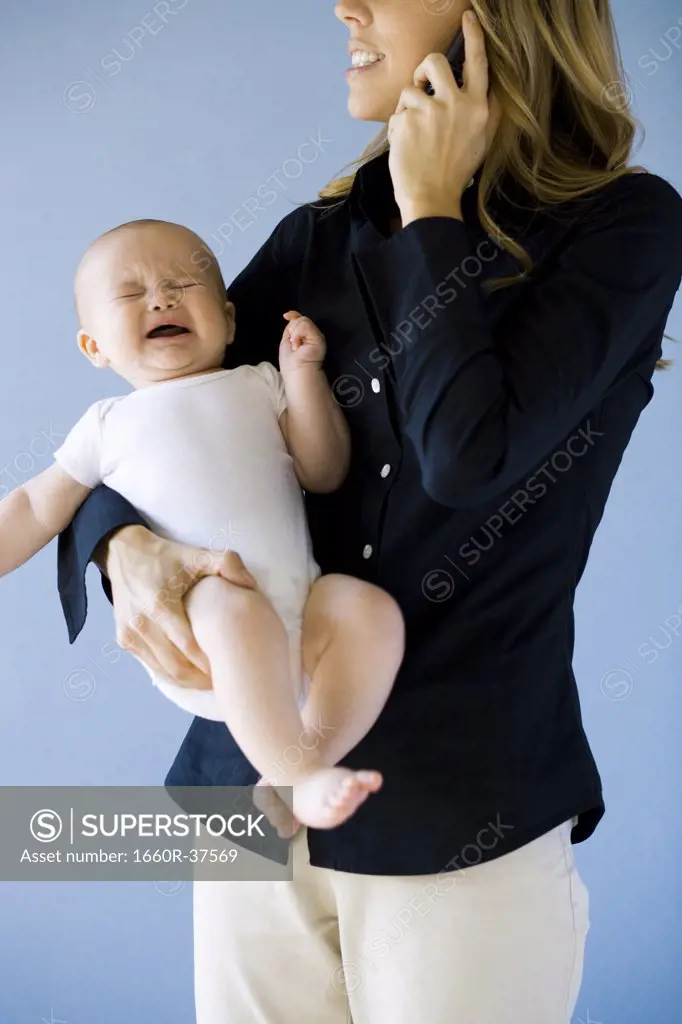 Woman on a cell phone holding a baby.