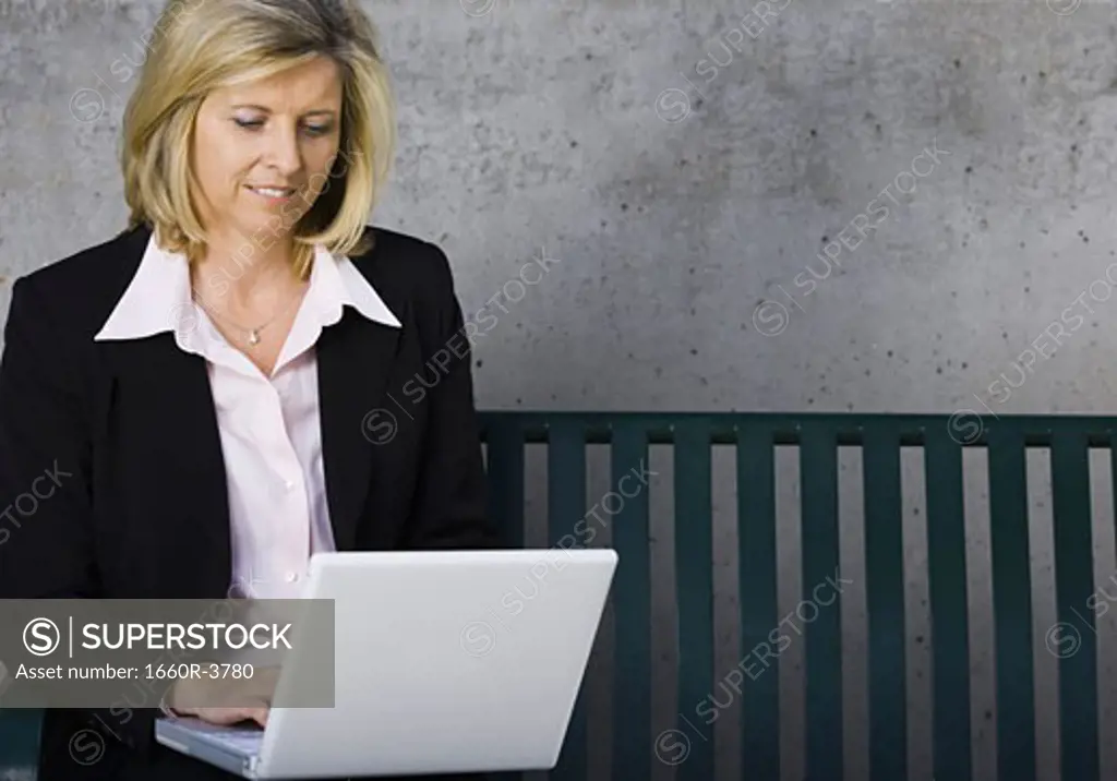 Businesswoman sitting on a bench and using a laptop