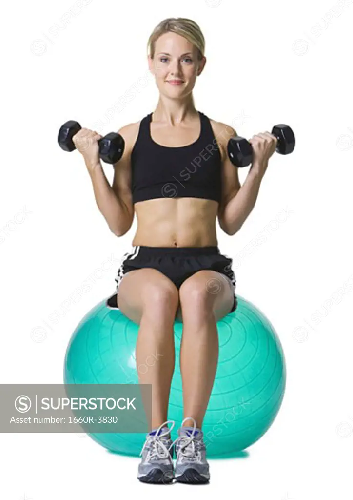 Portrait of a young woman sitting on a fitness ball holding dumbbells