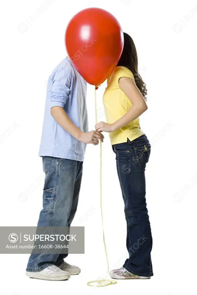 couple kissing behind a red balloon