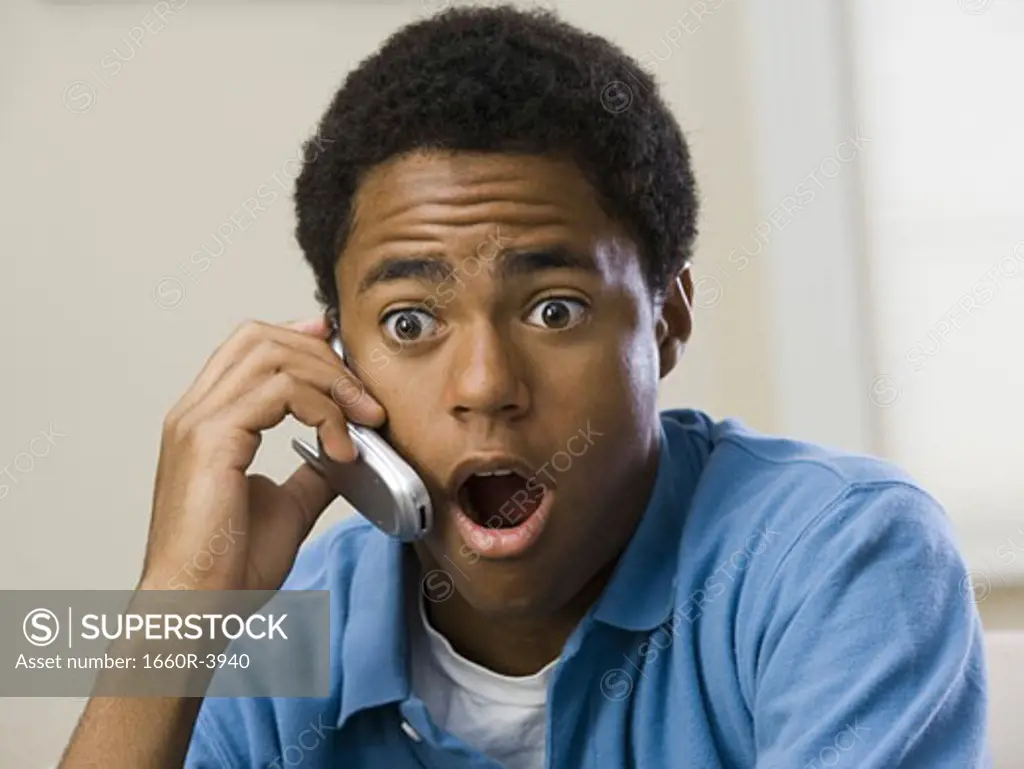 Teenage boy on a mobile phone with his mouth open, looking surprised