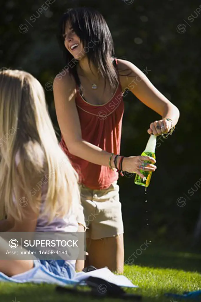 Low angle view of a young woman opening a beer bottle