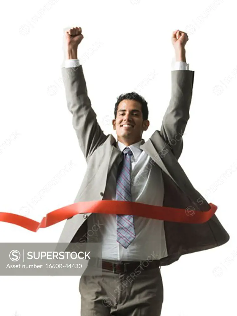 businessman crossing a finish line of a red ribbon with arms raised in the air triumphantly