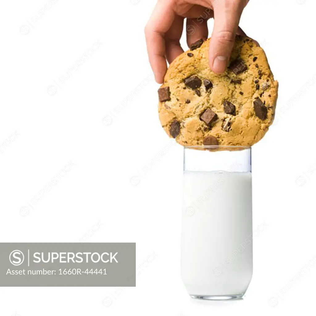 hand attempting to dunk a cookie thats too big into a glass of milk thats too small