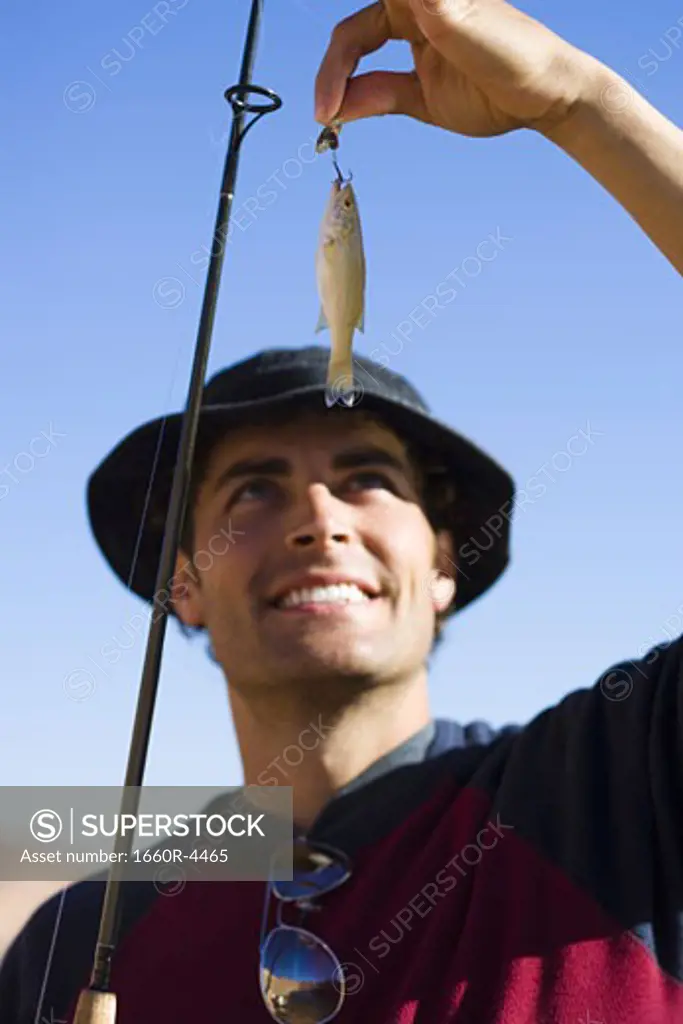Low angle view of a young man holding a fishing bait with a rod