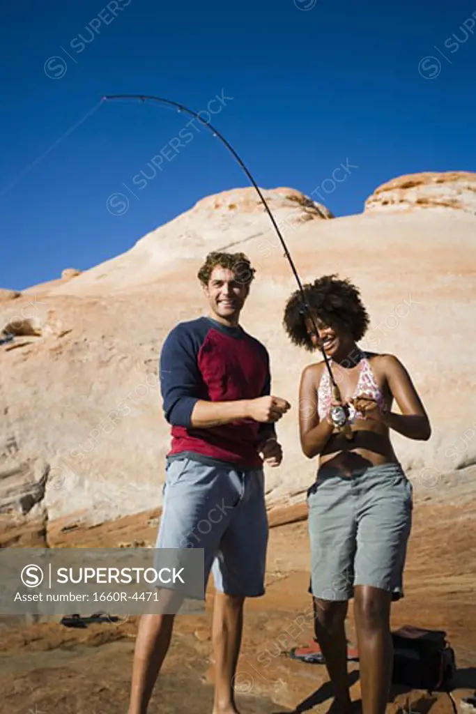 Young woman fishing with a young man standing beside her