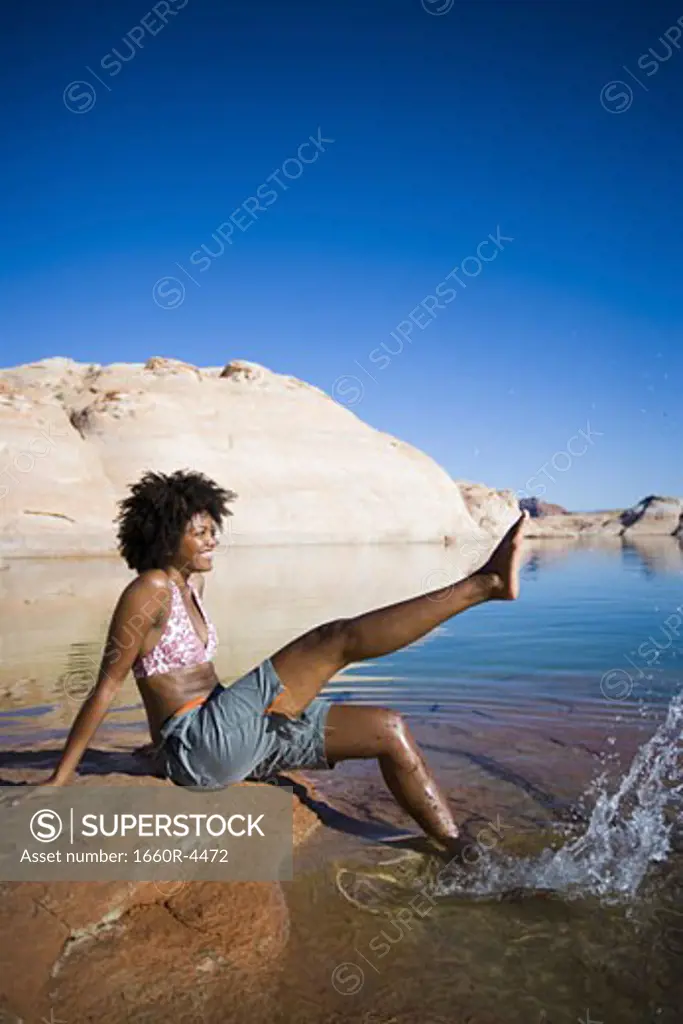 Profile of a young woman sitting on a rock and splashing water