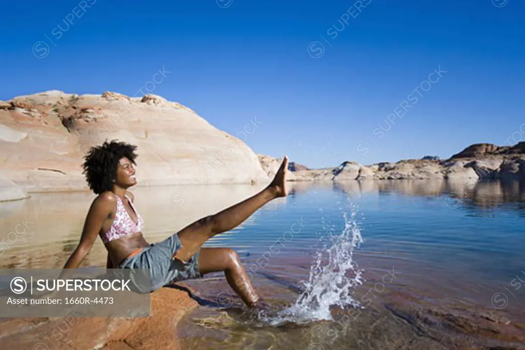 Profile of a young woman sitting on a rock and splashing water