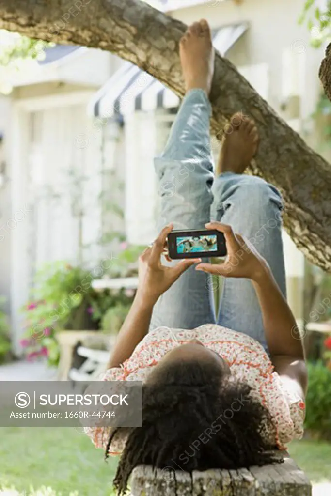 woman lying under a tree watching a portable media device