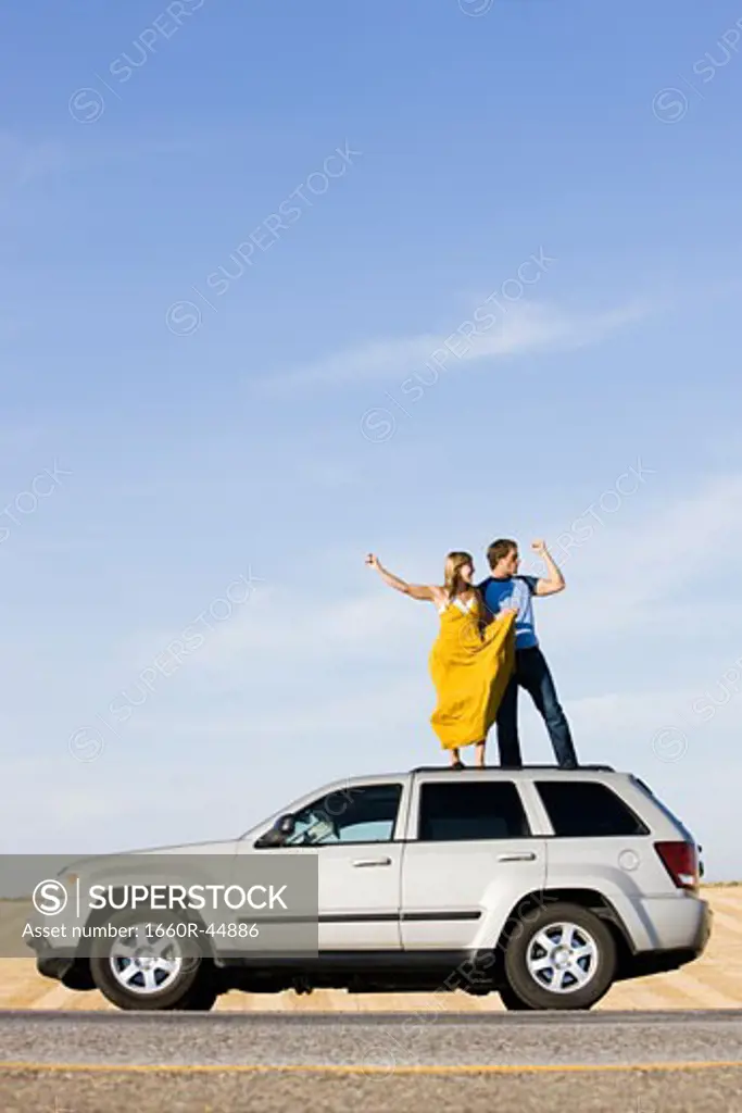 couple on the roof of their car on the side of the road